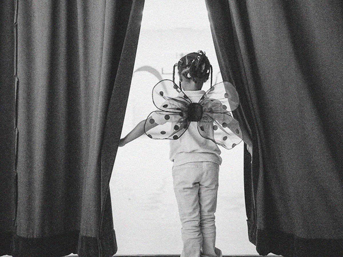 Young girl wearing butterfly wings opening curtains on a stage